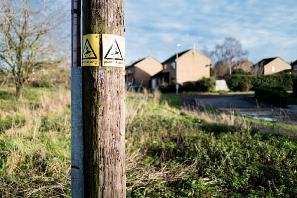 par de letreros de peligro de muerte unidos a un poste de telégrafo de madera que transporta electricidad a una urbanización cercana. - poste telegráfico fotografías e imágenes de stock