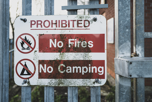 Shallow focus of a weathered, generic prohibited sign seen attached to a metal fence, leading to an out of bounds industrial area.