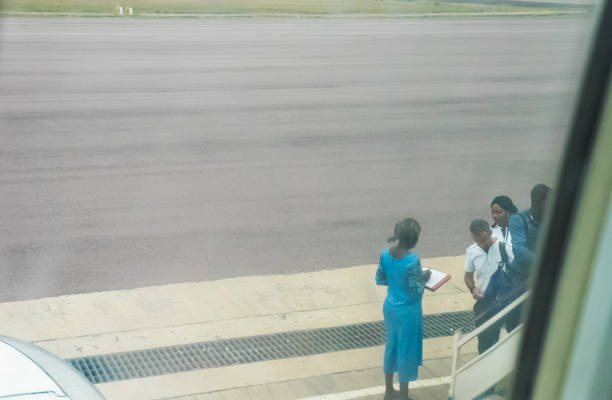 Congolese stewardess checks passenger entering stairs to airplane on airfield in Airport Brazzaville. stock photo