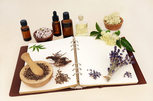 Lavender, elderflower and valerian herbs used in natural herbal medicine and aromatherapy as a sedative to treat anxiety, insomnia. With notebook and essential oil bottles. Natural health care concept.