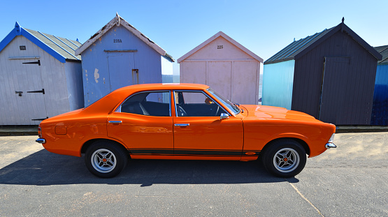 Felixstowe, Suffolk, England - May 06, 2018:  Classic Orange Ford Cortina MK3 Car Parked in front  of beach huts.