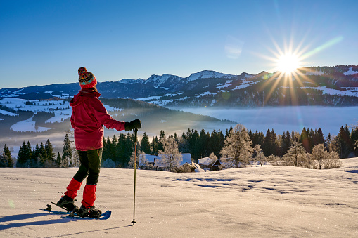 landscape with woman watching sunrise over the Nagelfluh mountain chain during a snowshoe hike in the Allgaeu Alps near Oberstaufen, Germany, Bavaria,