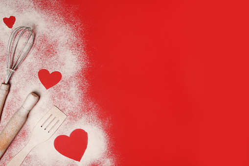 Valentine's Day Baking background. Hearts of flour with rolling pin on red table, copy space