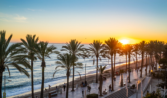 Marbella sunset beach in Playa de la Fontanilla in Malaga province of Spain. Fontanilla is the mostpopular beach with a promenade just downtown Marbella city and beautiful palm trees. Just beside the city marina dock.