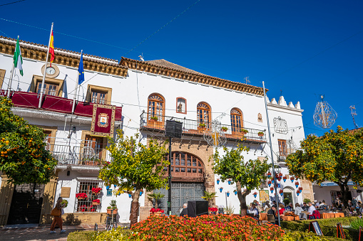 Marbella Town hall in Plaza de los Naranjos with flower pots in downtown Old Town in Costa del Sol of Malaga in Andalusian Spain. Plaza de los Narajos is the most visited square just in the center of the old town Marbella Casco Historico. Whitewashed facades and flower pots, beautiful gardens and orange trees which give the name to this square. This image was shot in Christmas 2021 then we can see the Christmas lights and decoration.