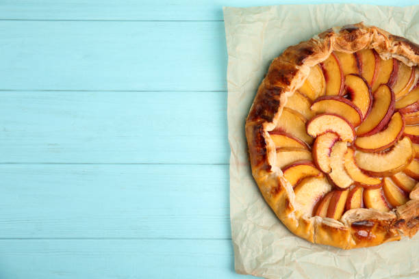 istock Delicious fresh peach pie on light blue wooden table, top view. Space for text 1362399468