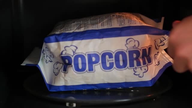 A man takes out a bag of ready-made popcorn from the microwave