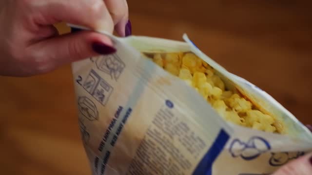 The girl opens a bag of hot, ready-made popcorn, stretching it to the sides.