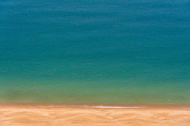 Blue sea water surface with waves on the sand tropical beach, top view. Sea water texture and background