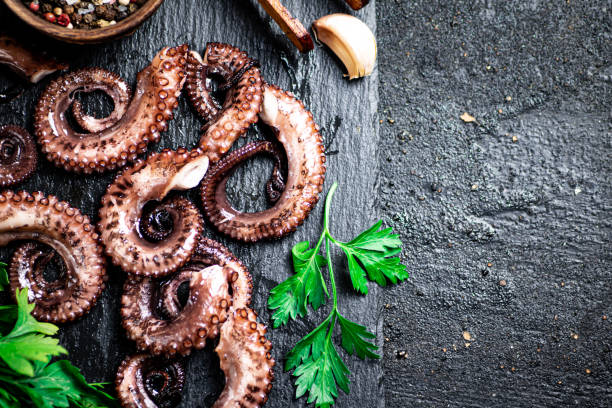 istock Pieces of fresh octopus on a stone board with greenery. 1362417474