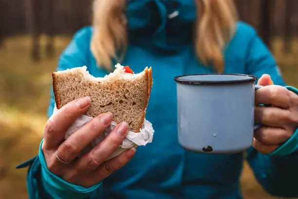 Woman eating sandwich and drinking hot drink. Hiker having lunch outdoors