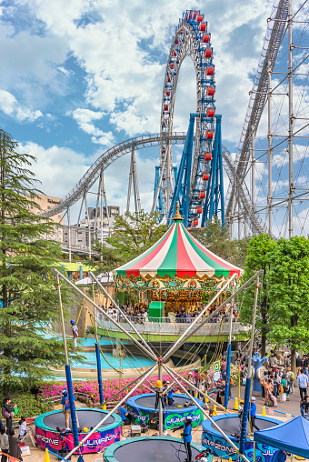 tokyo, japan - may 03 2019: Families enjoying trampoline and carousel in Laqua Tokyo Dome City Mall overlooked by Thunder Dolphin steel roller coaster and Big-O centerless non-rotating Ferris wheel.