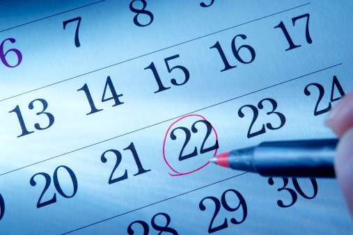 Blue tinted image of hand writing a red round mark of a calendar.