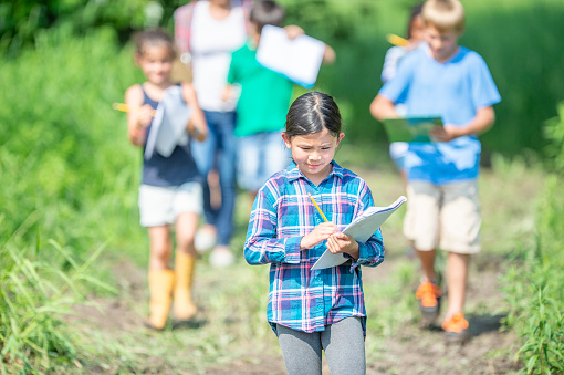 A small group of Elementary students walk together outside as they discover the ecosystem around them.  They are each dressed casually and holding clipboards as they record their findings.