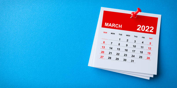 White Sticky Note With 2022 March Calendar And Red Push Pin On Blue Background stock photo