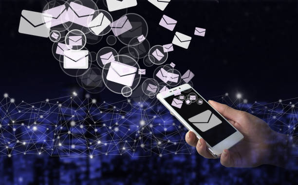 istock Sending email. Bulk mail. Hand hold white smartphone with digital hologram Email and sms sign on city dark blurred background. Business email concept. 1362428118