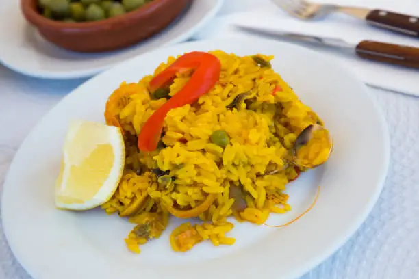 Appetizing racy paella with seafoods, green peas and bell pepper served with lemon slice.Traditional Valencian cuisine