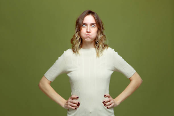istock Funny comic young woman making faces puffed up her cheeks looking with big eyes at camera on green studio background 1362432450