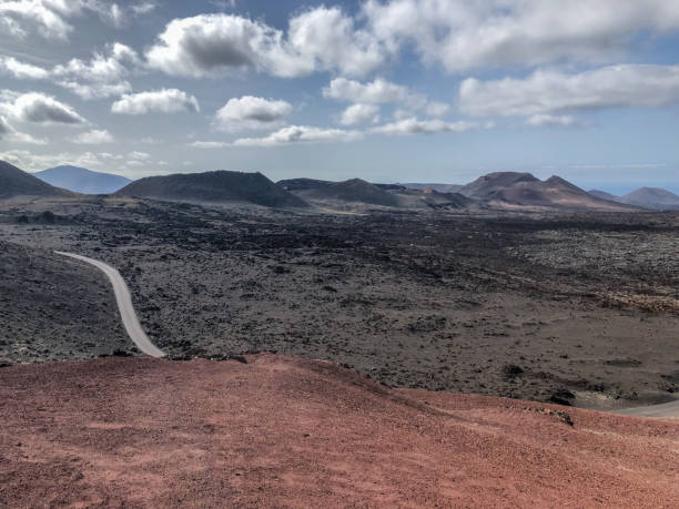 Timanfaya national park a volcanic landscape with a road along  with vulcans and montains on the background, at Lanzarote, Canary islands. Spain. stock photo