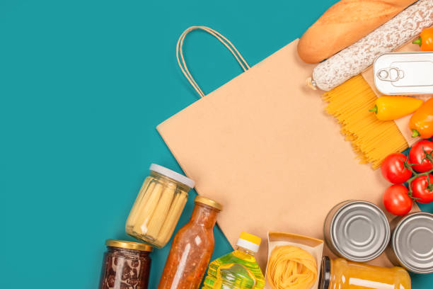 Food donations and paper bag on green background with copy space - pasta, fresh vegatables, canned food, baguette and other groceries. Food bank, food delivery concept. Mockup Food donations with paper bag on green background with copy space: pasta, fresh vegatables, canned food, baguette and other groceries. Mockup, food bank, food delivery concept. food bank stock pictures, royalty-free photos & images