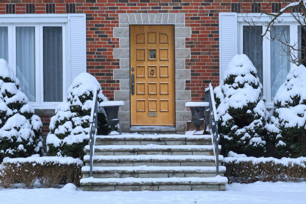 Traditional brick house with wood grain front door and snow covered shrubbery Traditional brick house with wood grain front door and snow covered shrubbery doorstep stock pictures, royalty-free photos & images