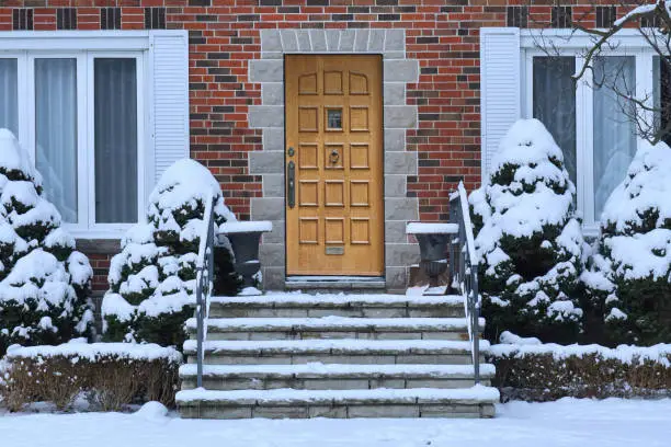 Traditional brick house with wood grain front door and snow covered shrubbery