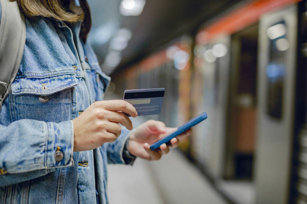 Woman's hand holding mobile phone and credit card at subway station Close up photo of woman's hand holding mobile phone while waiting for the train subway platform stock pictures, royalty-free photos & images