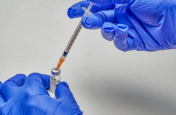istock Hands with blue gloves, holding a vial to which they are introducing a liquid with a syringe. 1362444187