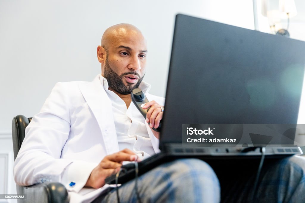 Black Male Radiologist Doctor Reading X ray Images on Laptop from Home A black male doctor working from home reads radiology X Rays on his laptop from home. Dictation Stock Photo