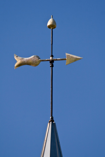 An arrow cross weather vane on top of a Christian Church.