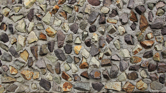 stone wall of different stones with concrete. Masonwork of raw stones. background of different colored natural stones walled up in concrete. background of small stones with copy space for text. Stone wall