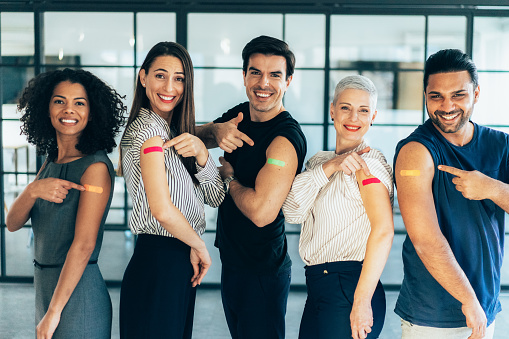 Group of multiracial people looking at camera pointing at their arm with a bandage after getting the covid-19 vaccine