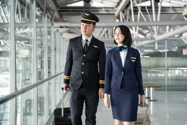 商業客室乗務員またはホストレスとパイロット職業の概念。アジアの旅客機のパイロットとエアホステスは、笑顔と幸せで飛行機に空港ターミナルで一緒に歩いて話します。 - cabin crew pilot airport walking ストックフォトと画像