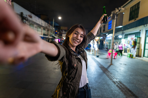 Asian woman backpacker use mobile phone selfie, take picture in city. Beautiful woman tourist traveler travel alone on street, use smartphone record vlog on holiday vacation trip in Thailand at night.