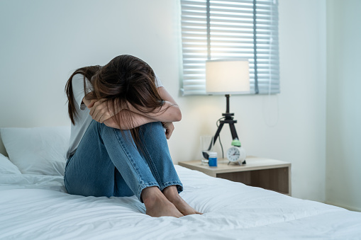 Asian beautiful upset depressed girl sitting alone on bed in bedroom. Attractive unhappy young woman feel sad lonely and upset with life problem and trying to hurt herself in dark night room at home.