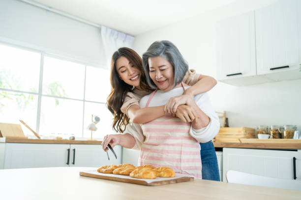 belle famille asiatique, la jeune fille regarde la vieille mère cuisiner dans la cuisine. belle femme aiment passer du temps libre et étreindre la mère âgée âgée faire un croissant sur la table à la maison. relation d’activité - mother cooking daughter child photos et images de collection