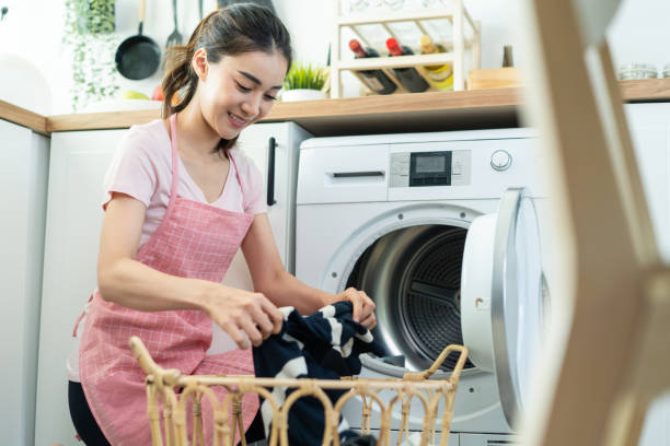 Asian beautiful woman put dirty clothes to washing machine in house. Attractive girl wear apron sit on floor, feel happy to loads laundry in washer appliance at home. Domestic-House keeping concept. la hermosa mujer asiática puso ropa sucia a la lavadora en la casa. chica atractiva usar delantal sentarse en el suelo, sentirse feliz de cargas de lavandería en el electrodoméstico de la lavadora en casa. concepto de mantenimiento de la casa doméstica