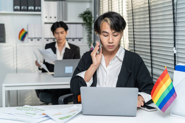 Asian handsome businessman gay people working in office with happiness. Attractive male lgbtq collogues in formal wear sitting on table, use laptop computer with gay pride and confidence at workplace. Asian handsome businessman gay people working in office with happiness. Attractive male lgbtq collogues in formal wear sitting on table, use laptop computer with gay pride and confidence at workplace. transgender person in office stock pictures, royalty-free photos & images