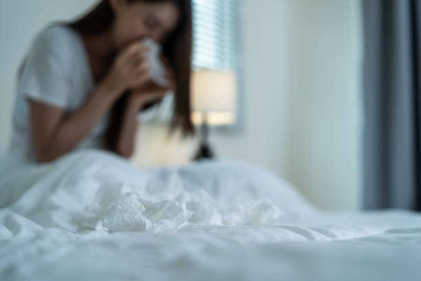 Asian sick girl in pajamas wake up from sleep at night sneezing on bed. Attractive young woman feeling bad and suffer from allergy, put tissue cover her nose while sneezes during bedtime in house. niña asiática enferma en pijama se despierta del sueño por la noche estornudando en la cama. mujer joven atractiva que se siente mal y sufre de alergia, se pone pañuelos de papel que cubren su nariz mientras estornuda durante la hora de acostarse en ca