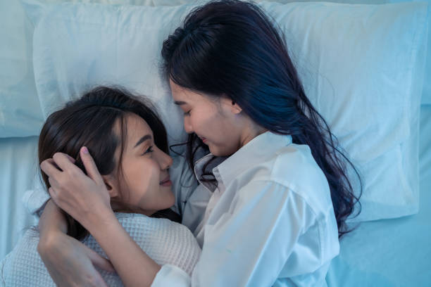istock Asian beautiful lesbian couple lying down on bed and hugging each other. Attractive romantic girl friend in pajamas spending night leisure time together in bedroom. Homosexual freedom pride concept. 1362491421