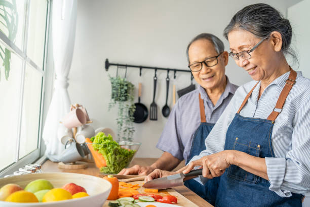 la coppia di anziani asiatici amorevole indossa grembiule e cucina in cucina. attraente vecchio forte e donna nonno indossare occhiali godere di attività di vita pensionistica a casa. concetto di relazione familiare. - chinese ethnicity foto e immagini stock