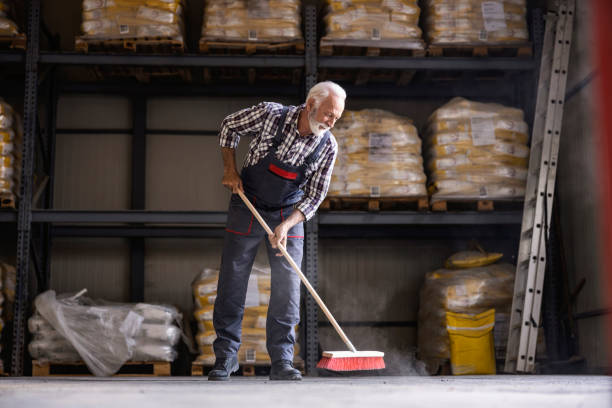 jornada laboral en fábrica. un trabajador senior de la fábrica está escobando la nave de la fábrica. - dust dusting cleaning broom fotografías e imágenes de stock