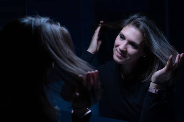 uma jovem adulta olhando para o rosto através do espelho antes da maquiagem - mirror women kissing human face - fotografias e filmes do acervo