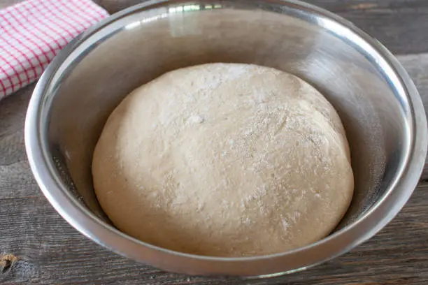 Fresh and raw yeast dough finished and ready to bake in a bowl on rustic and wooden table background