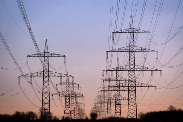 High voltage pylons in the evening sun Large group of electricity pylons and moody sky. energy crisis stock pictures, royalty-free photos & images