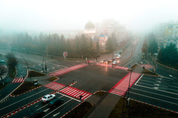 Color image depicting a high angle view of the city of Deva, a town in the Transylvania region of Romania. It is a misty morning and many cars are driving on the main intersection in the center of town.