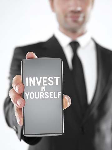 Businessman holding a mobile phone with ‘Invest in yourself’ text  on the screen
