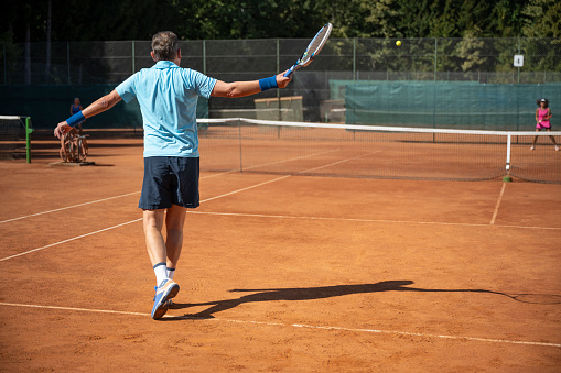 Active senior couple playing tennis on a clay court during sunny day.