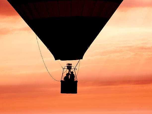 Hot air baloon silhoette, shot in the sunrise with two people inside the basket.