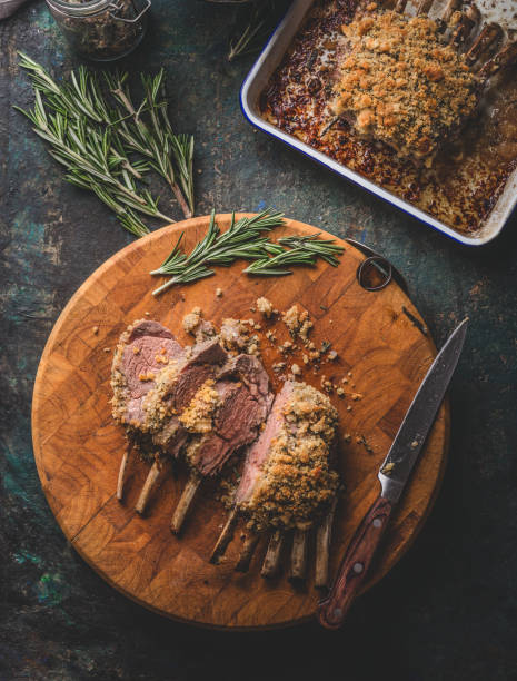 Tasty medium rare roasted lamb ribs with crust on wooden cutting board with rosemary and knife. stock photo